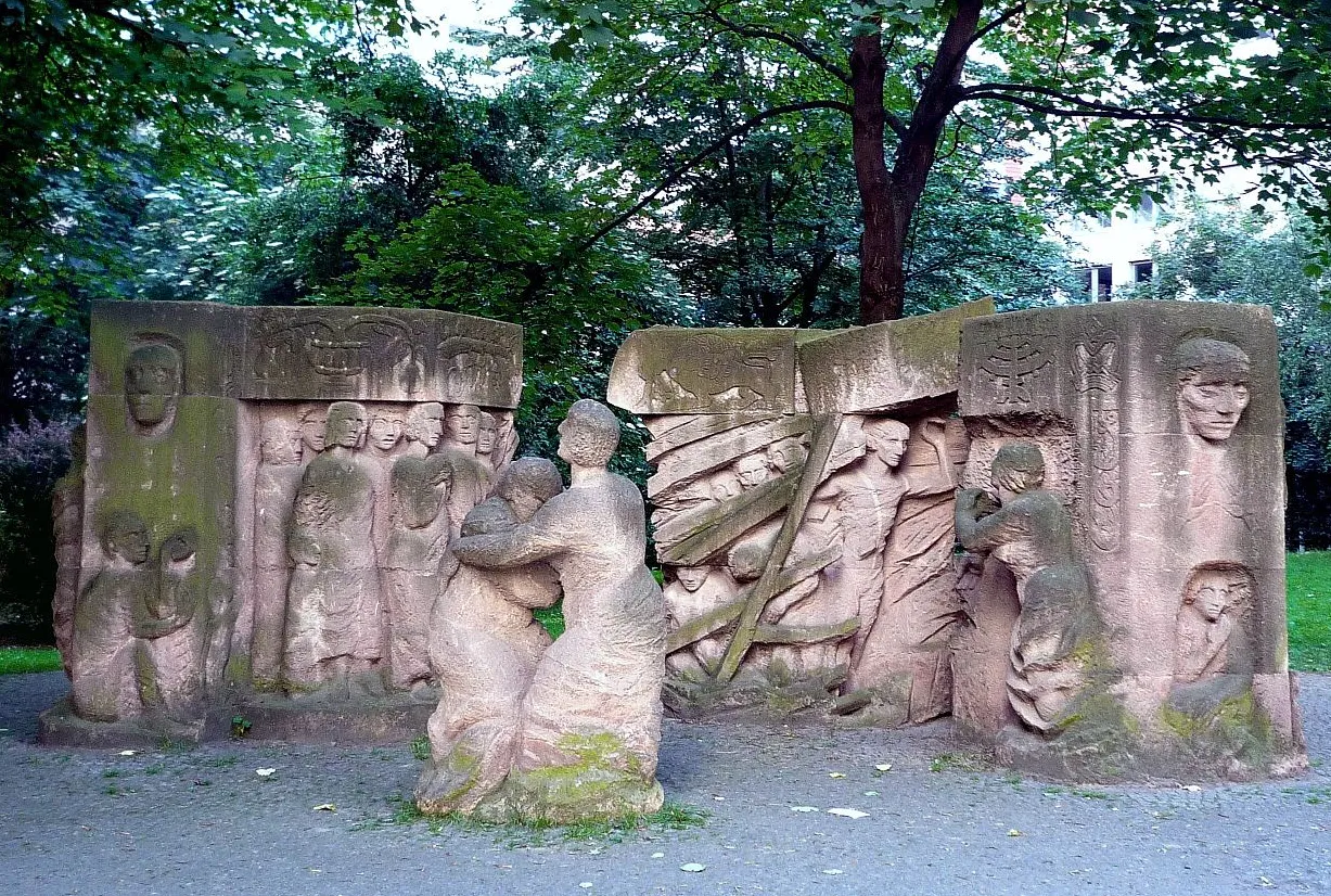 Stone sculpture of two women embracing while two additional stone sculptures depict men and women wrapped in cloth with looks of despair